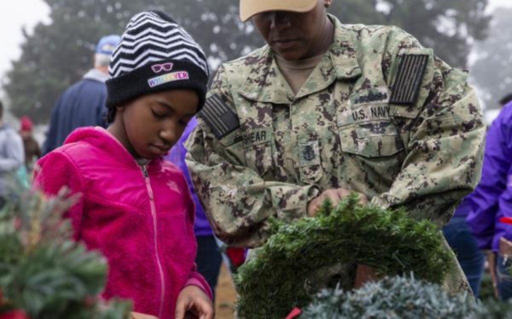 A girl and a Navy service member lay a wreath during Wreaths Across America