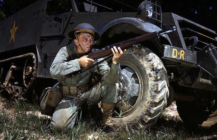 A soldier crouches with an M1 Garand, a precursor to the M16