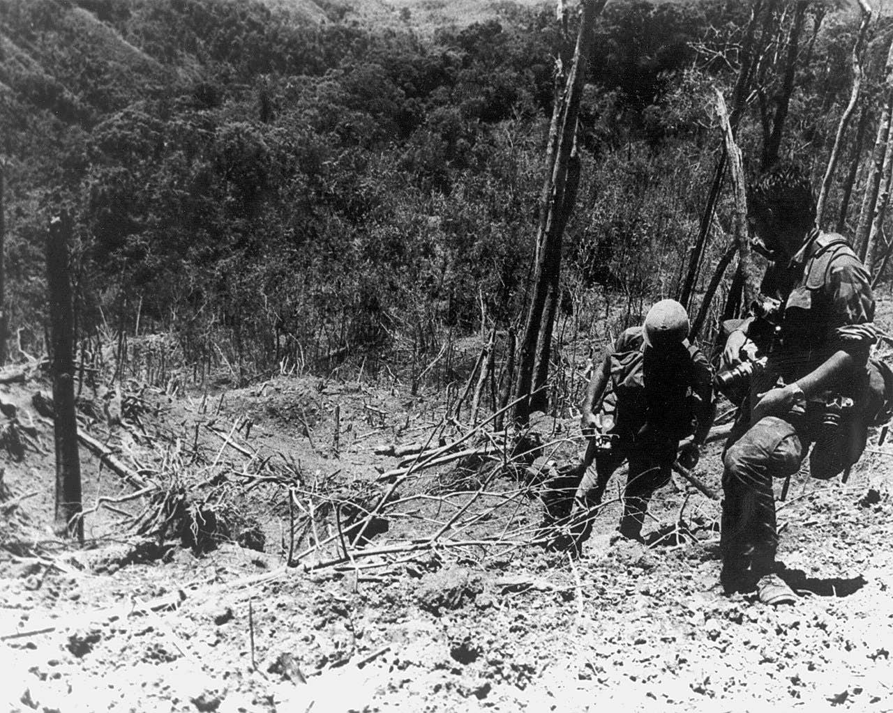 A U. S. Army Photographer and assistant climbing through the devastated landscape on Dong Ap Bia after the battle. (Melvin Zais Photograph Collection). (Photo Credit: USAMHI)