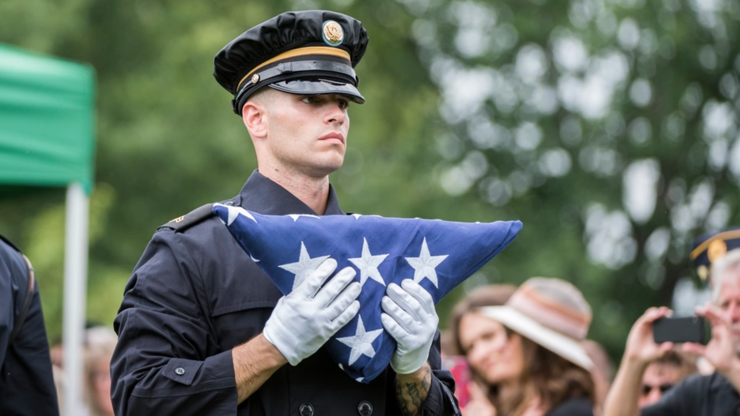 A soldier from the U.S. Army Honor Guard carries a U.S. flag during the Full Honors Group Funeral Service for U.S. Army Air Forces Airmen missing from World War II in Section 60 of Arlington National Cemetery, Arlington, Virginia, June 27, 2018. Laid to rest were Airmen Tech. Sgt. John Brady; Tech. Sgt. Allen Candler, Jr.; 1st Lt. John Liekhus; Staff Sgt. Robert Shoemaker; and Staff Sgt. Bobby Younger.