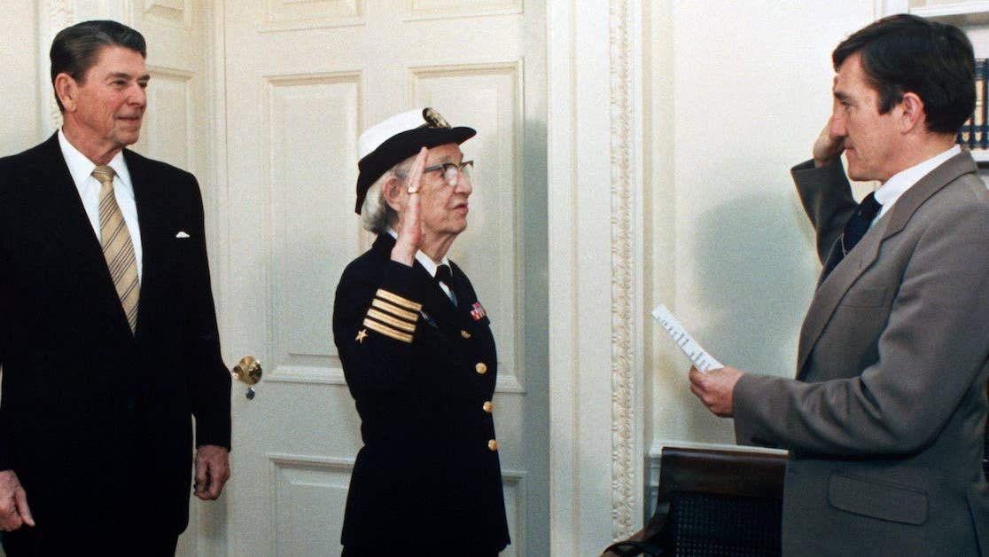  Secretary of the Navy, John Lehman, right, promotes Capt. Grace Hopper to the rank of commodore in a ceremony at the White House. President Ronald Reagan is at the left. (Wikimedia Commons)