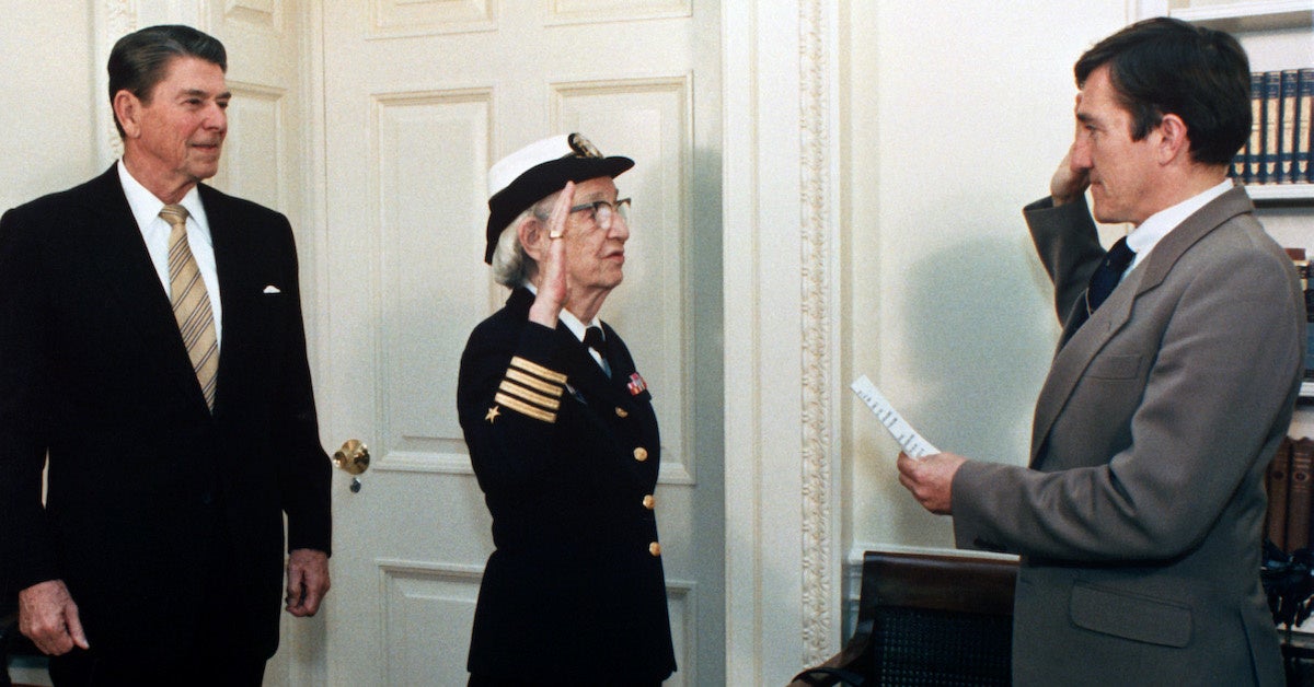  Secretary of the Navy, John Lehman, right, promotes Capt. Grace Hopper to the rank of commodore in a ceremony at the White House. President Ronald Reagan is at the left. (Wikimedia Commons)
