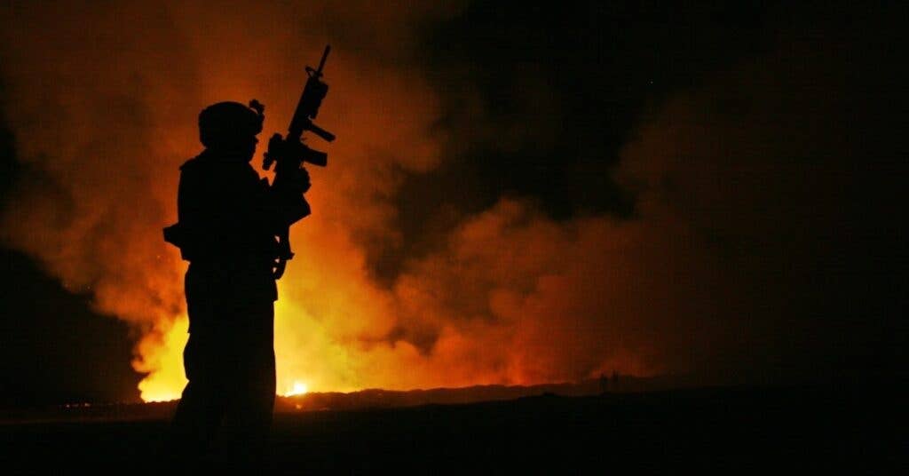 <em>A Marine watches over a burn pit at Camp Fallujah, Iraq (U.S. Marine Corps)</em>