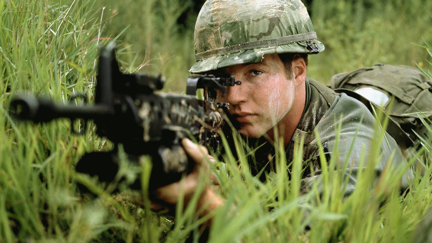 A US Army soldier aims an M16A1 rifle equipped with an M203 grenade launcher.