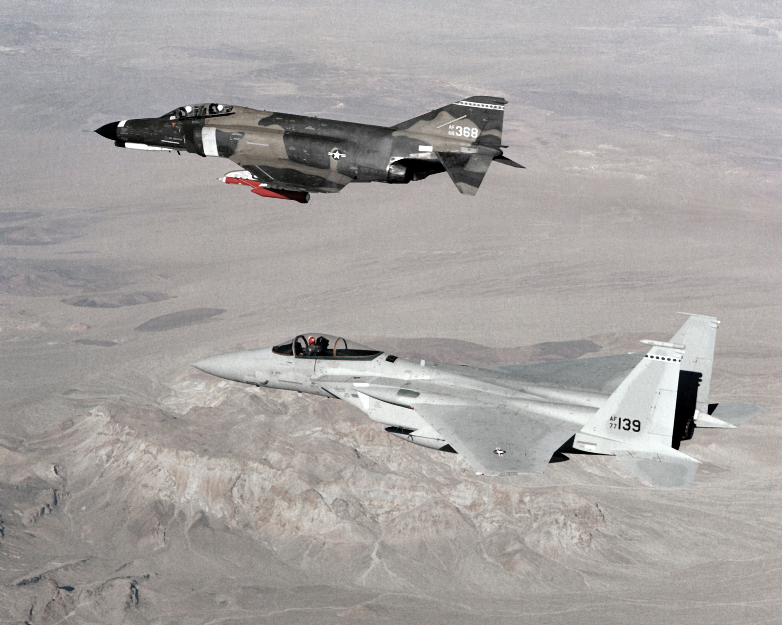 An air-to-air left side view of an F-4 Phantom II aircraft in formation with an F-15 Eagle aircraft.  The F-4 has a tow target mounted under its left wing.