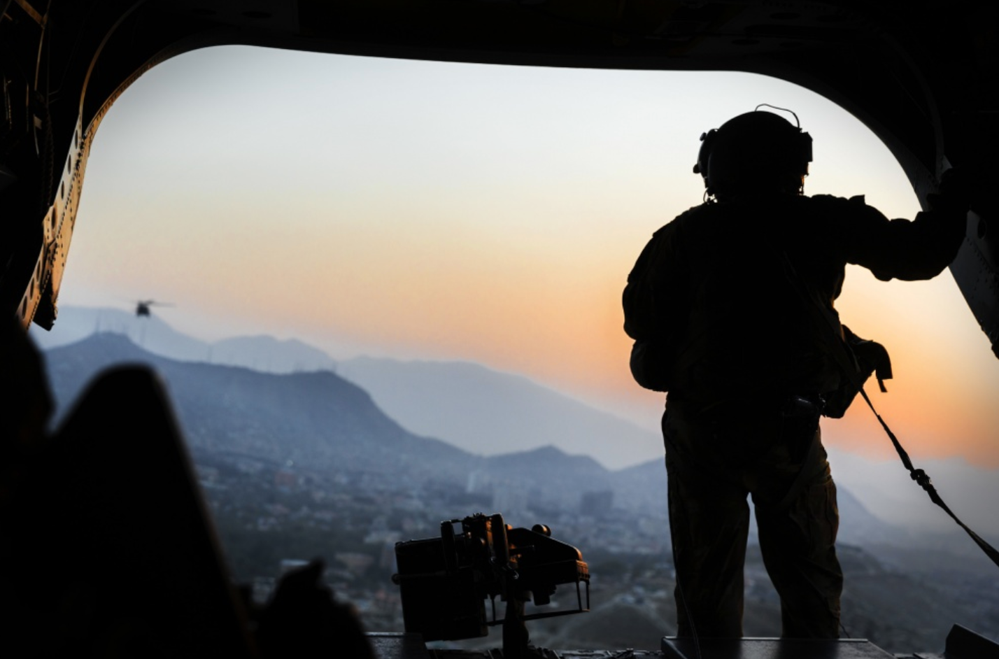 A United States Army loadmaster stands on the rear ramp of a CH-47F Chinook and watches the sunset as it flies over Kabul, Afghanistan. US Army photo.