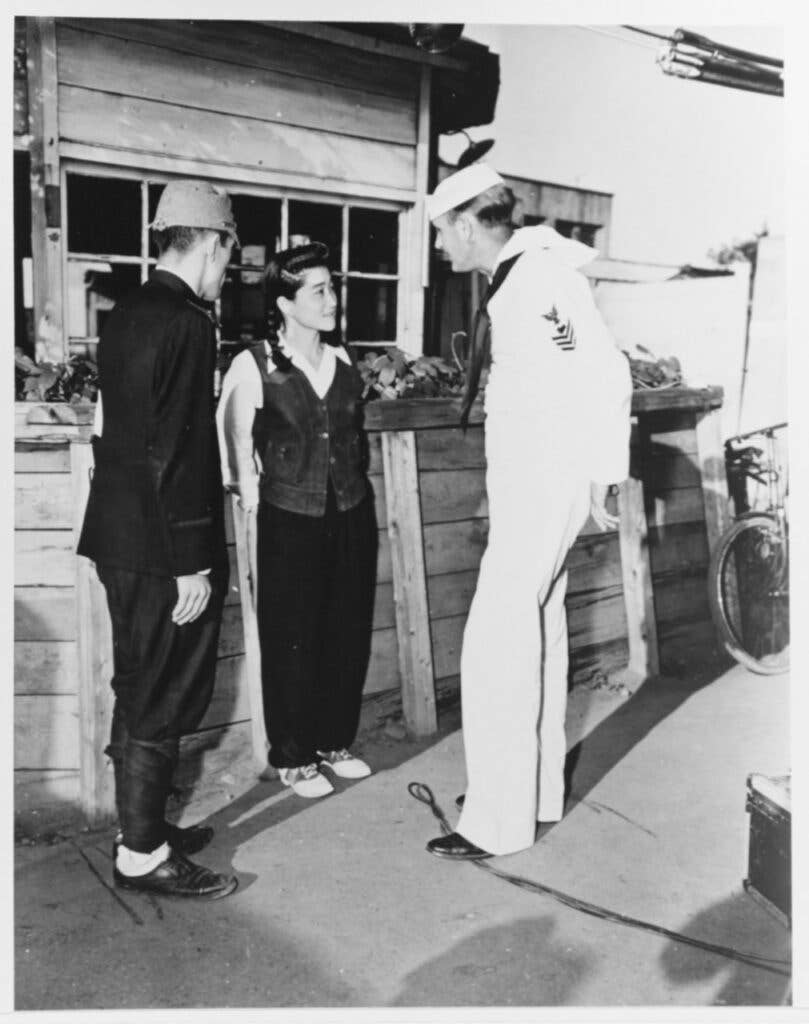 Talking with Photographer's Mate 1st Class Thomas Gode and a Japanese policeman outside her Tokyo home during the making of a CinCPAC newsreel 9 September 1945 (National Archives)