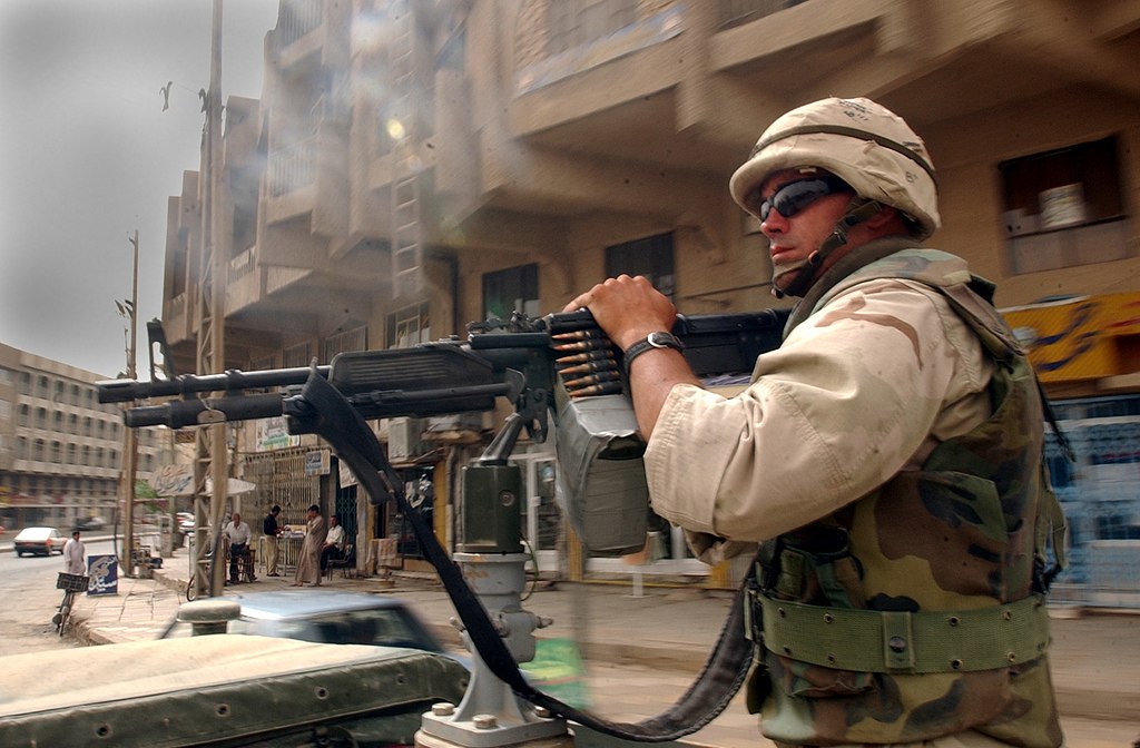 A U.S. Navy Seabee mans a vehicle-mounted machine gun while travelling through Al Hillah, Iraq in May 2003.