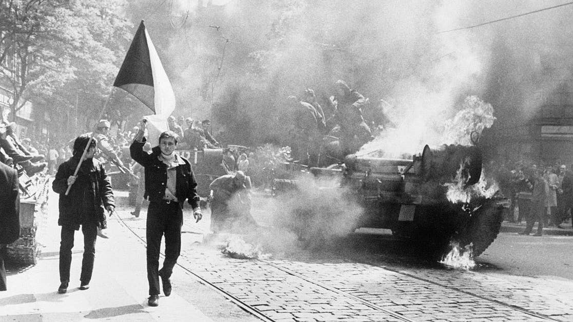 Czechoslovaks carry a national flag past a burning soviet tank in Prague. (CIA.gov)