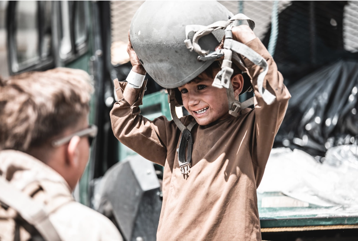 A U.S. Marine assigned to Special Purpose Marine Air-Ground Task Force – Crisis Response – Central Command hands a helmet to a child awaiting evacuation at Hamid Karzai International Airport, Afghanistan, Aug. 22, 2021. (U.S. Marine Corps photo by Gunnery Sgt. Melissa Marnell).