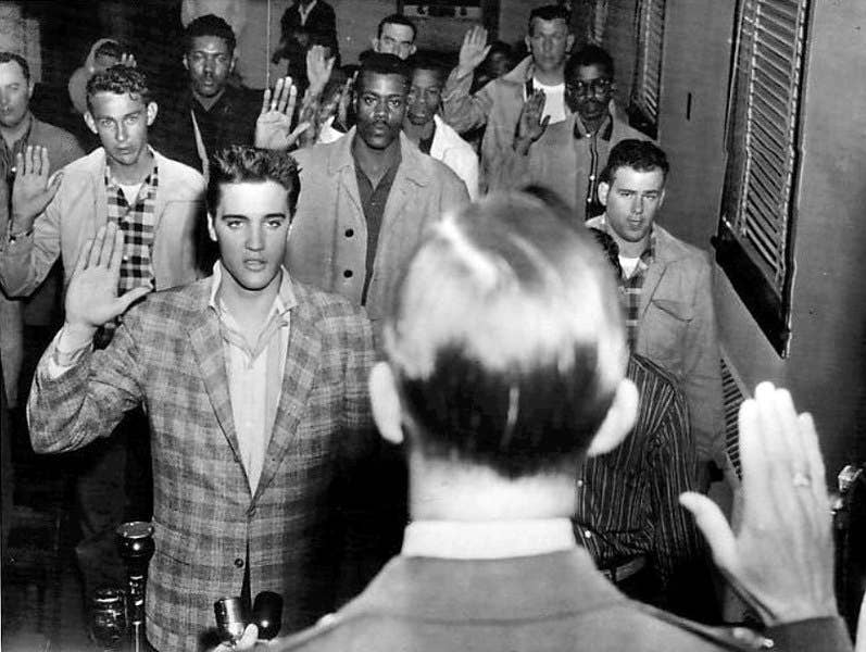 Photo of Elvis Presley and a roomful of other young men being sworn into the US Army as part of their induction at Fort Chaffee, Arkansas. (Wikimedia Commons)