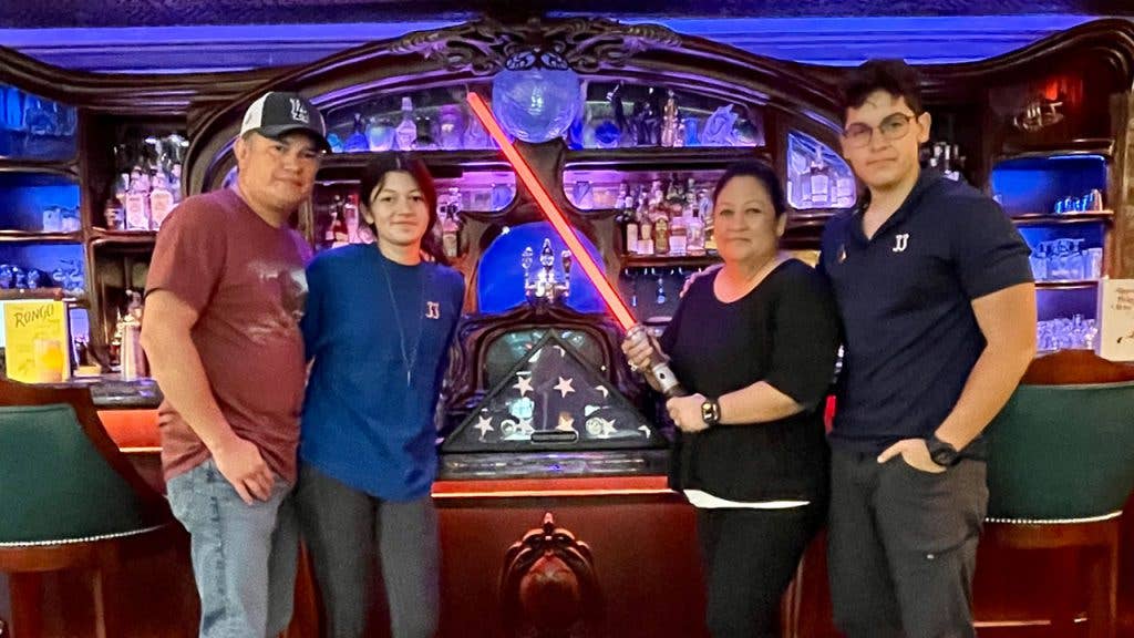 <em>The Lopez family at Club 33 with the replica of Hunter's lightsaber and the flag (Disney Parks)</em>