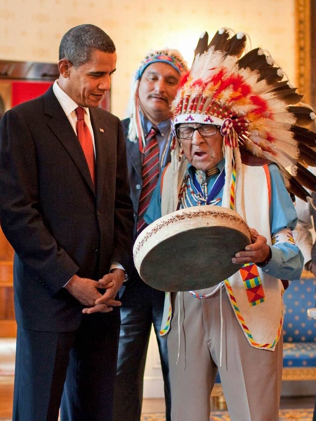Joe Medicine Crow in full feathered headdress plays a drum for U.S. President Barack Obama. (Wikimedia Commons)
