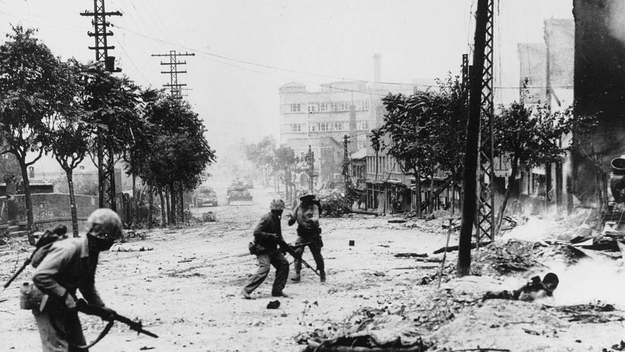 U.S. Marines engaged in street fighting during the liberation of Seoul. Note M-1 rifles and Browning Automatic Rifles carried by the Marines, dead Koreans in the street, and M-4 "Sherman" tanks in the distance. (Naval History and Heritage Command)