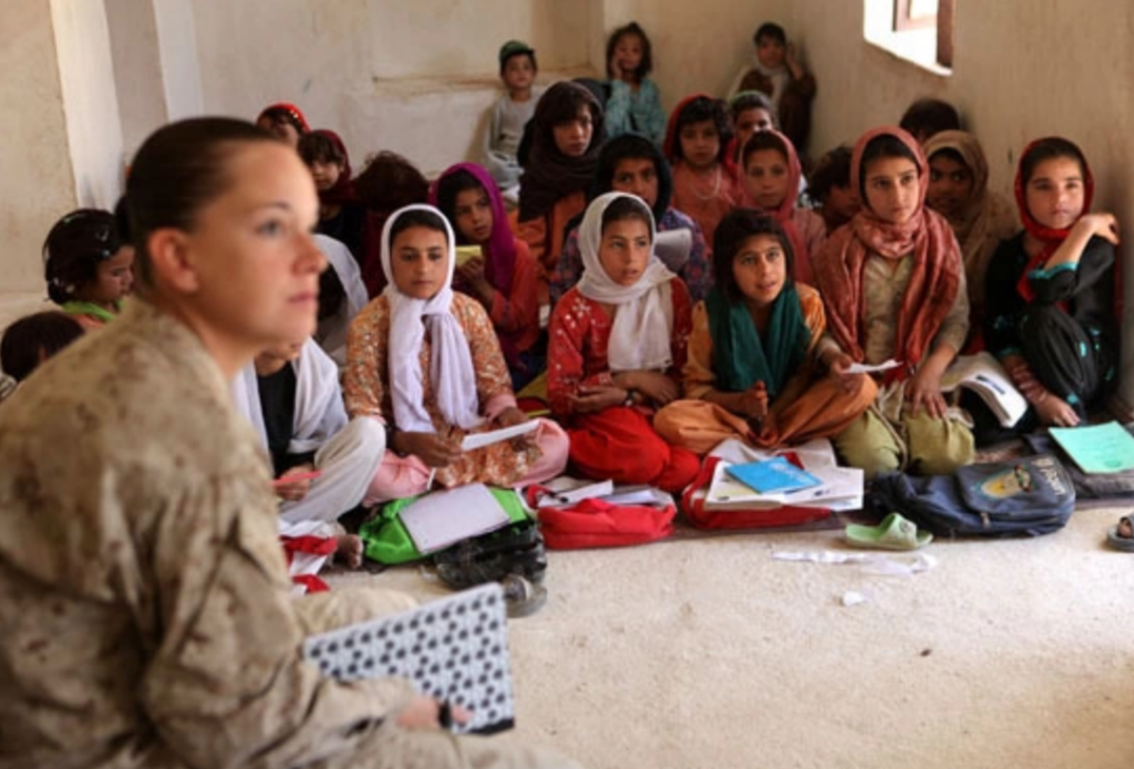 Lance Cpl. April Whitham, Now Zad female engagement team leader, listens as Dawood, the girls' teacher writes three questions on the chalkboard in Now Zad, Afghanistan. The girls, who range in ages from five to 12 have only one male teacher and only regularly attend school 3 hours a day.