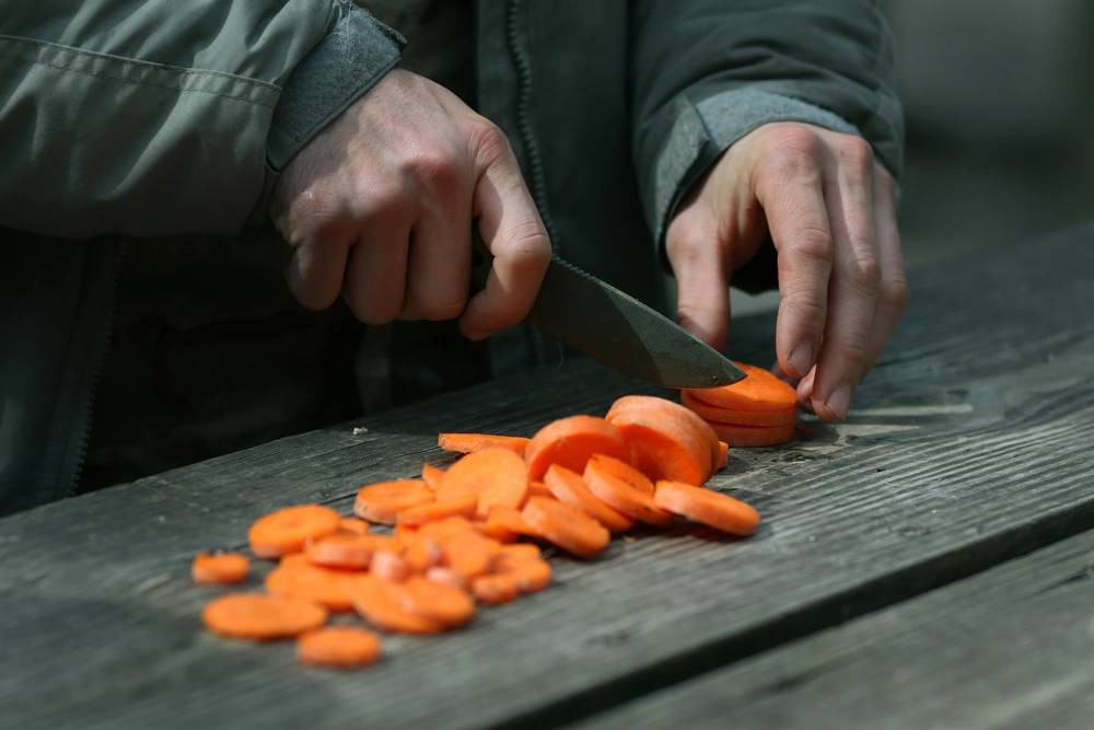 A sudent from the U.S. Army John F. Kennedy Special Warfare Center and School, cuts carrots as part of food preparation training during the survival phase of Survival Evasion Resistance and Escape Level-C training (SERE) at Camp MacKall, North Carolina, Feb. 27, 2019.  (U.S. Army photo by K. Kassens)