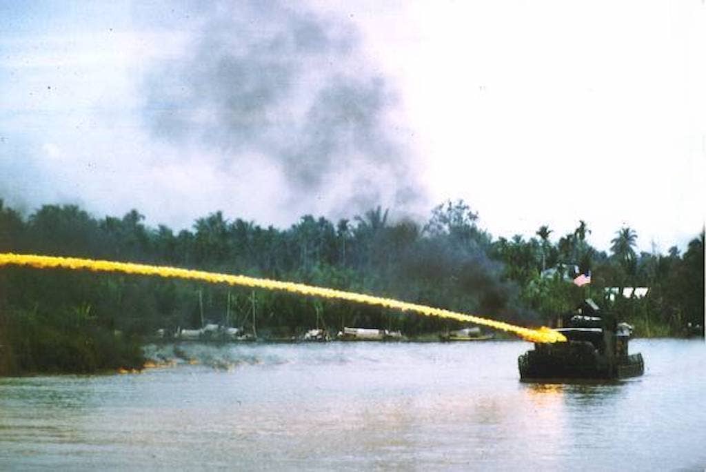 Riverboat of the U.S. Brown-water navy deploying an ignited napalm mixture from a riverboat-mounted flamethrower in Vietnam.