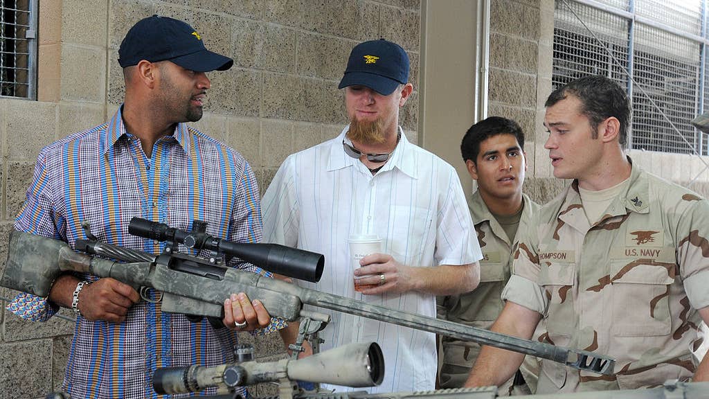 Special Warfare Operator 1st Class Thompson explains details of an Mk 15 sniper rifle to major league baseball players Albert Pujols and Ryan Franklin during a tour of Naval Special Warfare facilities.