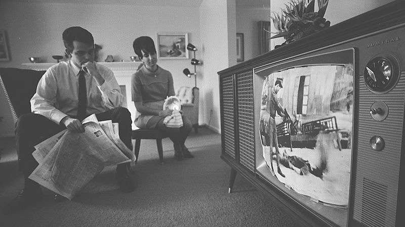 An American man and woman watching footage of the Vietnam War on a television in their living room.