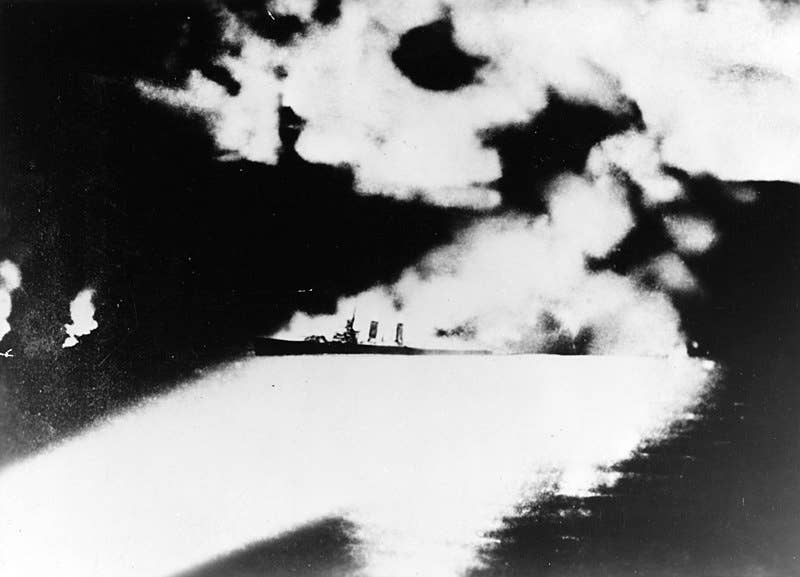 The U.S. Navy heavy cruiser USS <em>Quincy</em> (CA-39) photographed from a Japanese cruiser during the Battle of Savo Island, off Guadalcanal, 9 August 1942. <em>Quincy</em>, seen here burning and illuminated by Japanese searchlights, was sunk in this action.
