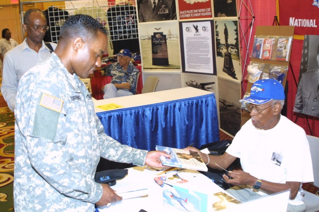 <em>Jefferson signs a copy of his book at the 35th Annual Tuskegee Airmen National Convention (U.S. Air Force)</em>