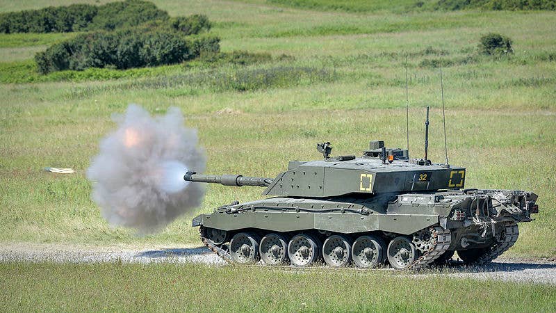 A Challenger 2 firing its main armament during an exercise. The shell is visible to the left of the smoke cloud.