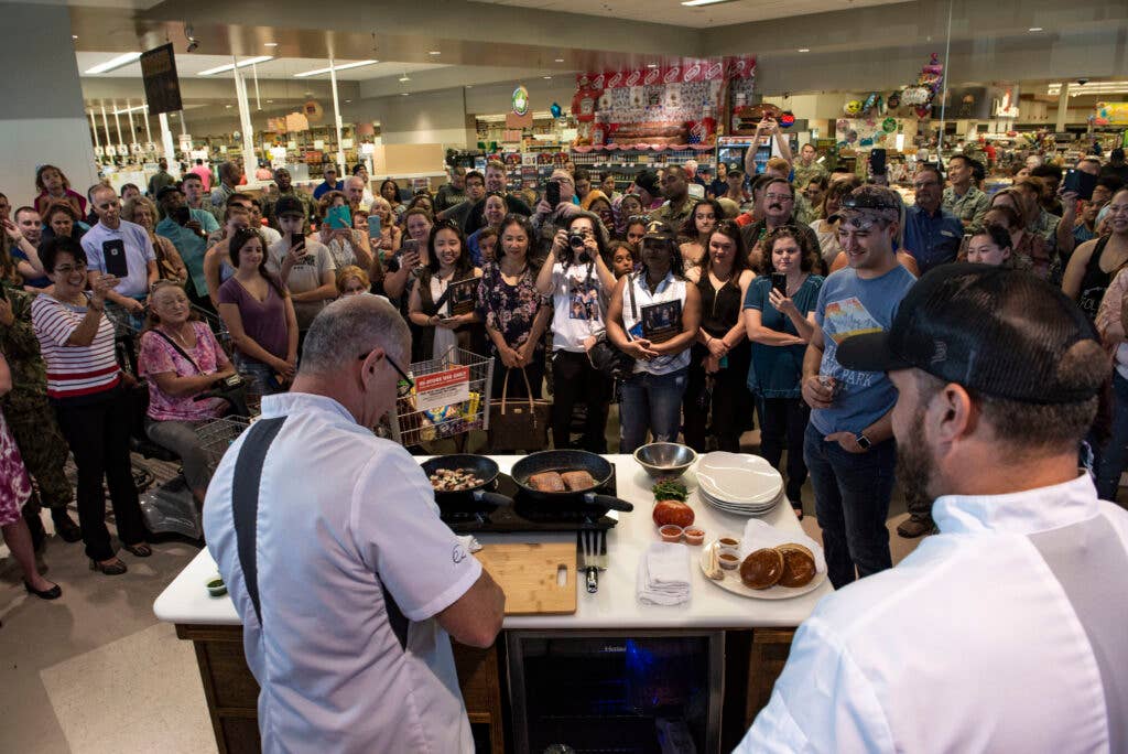 Members of team Nellis look on as celebrity chef Robert Irvine prepares a dish at the Nellis Commissary on Nellis Air Force Base, Nev., July 19, 2019. (U.S. Air Force photo by Senior Airman Julian W. Kemper)