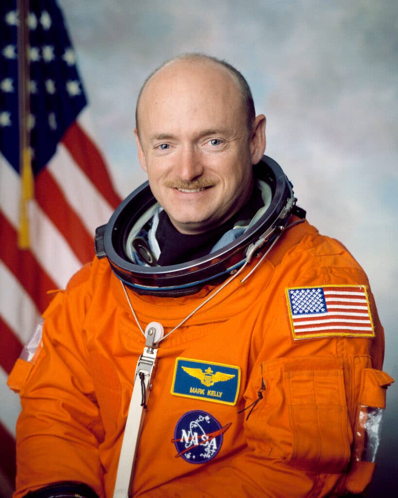 Official Portrait of Astronaut Mark E. Kelly. Kelly is wearing the orange Launch and Entry Suit (LES) with an American flag in the background.

NASA Identifier: JSC2001-01916