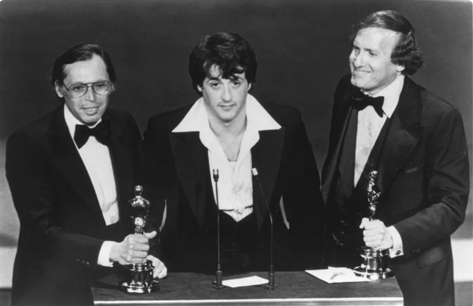 Winkler (left) with Sly Stallone and Robert Chartoff (right), receiving their Oscars for Rocky. Public domain.
