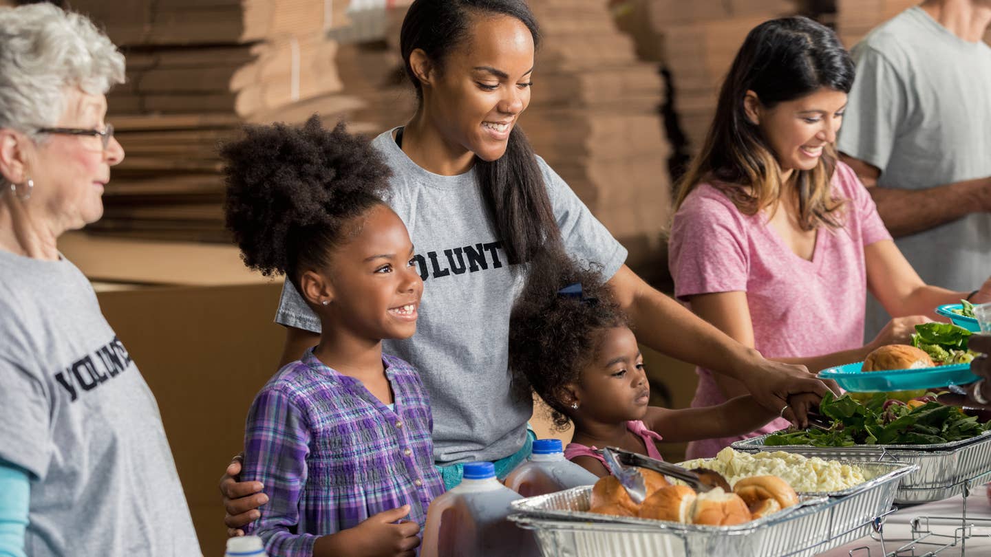 African American mother and her two daughters serve meals to the homeless with their diverse family.