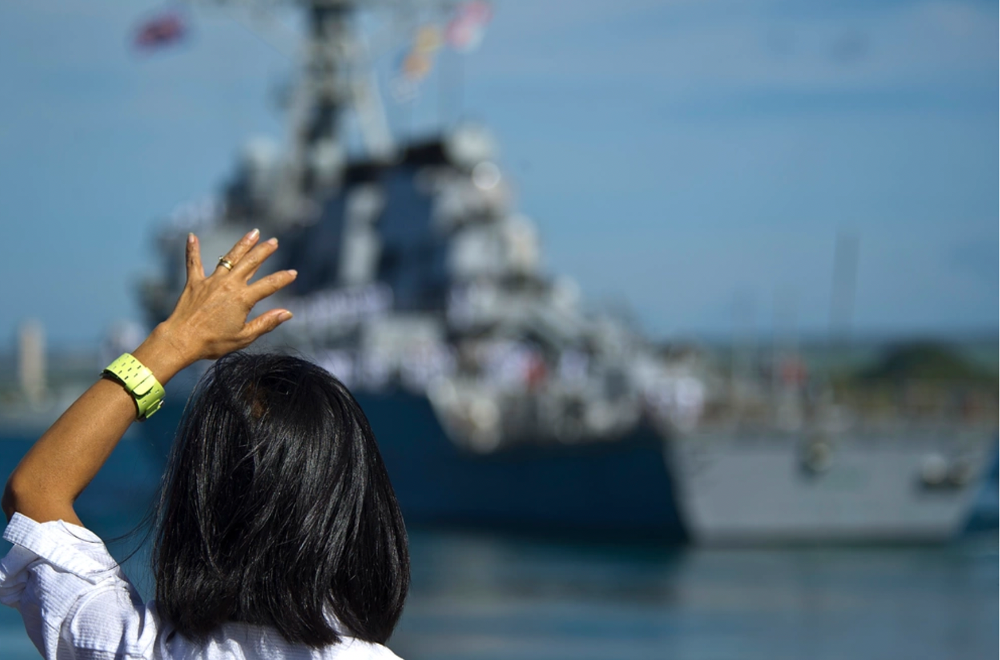 A military spouse waves goodbye to a ship