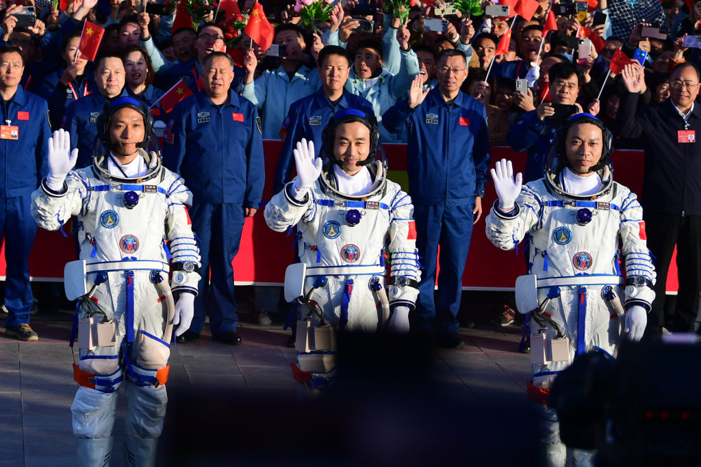 Three Chinese astronauts in space suits waving at crowd.