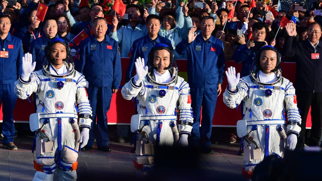 Three Chinese astronauts in space suits waving at crowd.