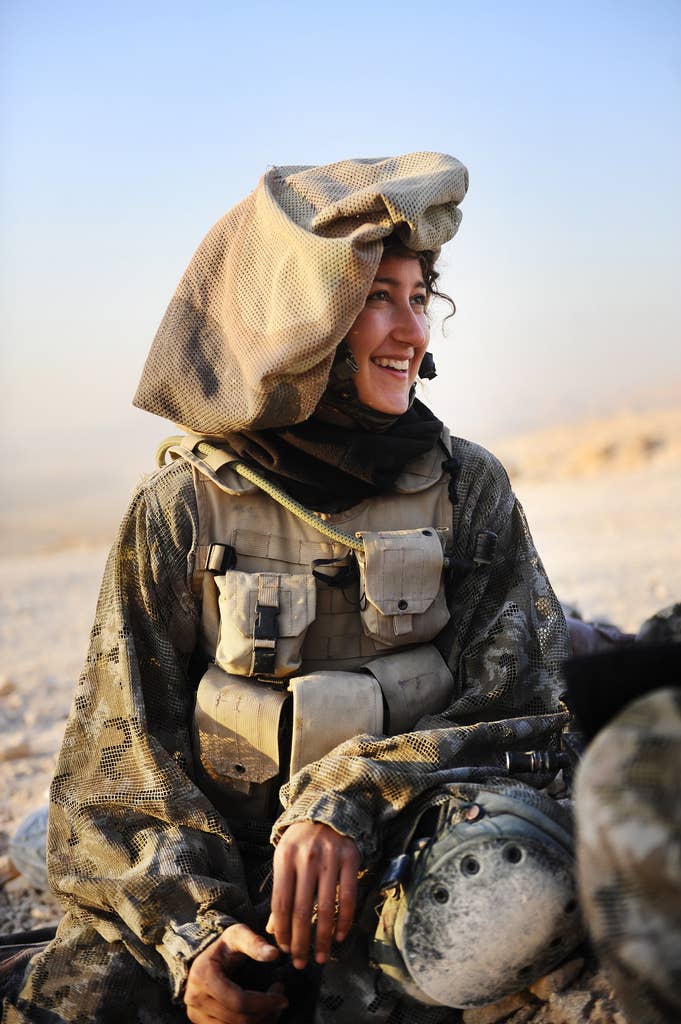 A female IDF soldier sitting and wearing a mitznefet on her helmet.