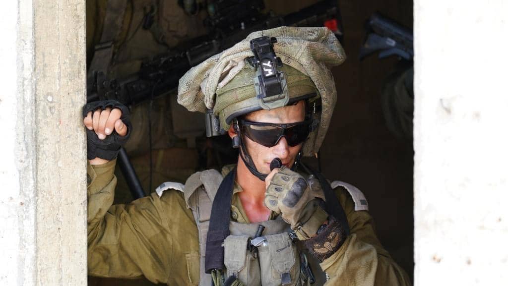 A IDF soldier wearing a mitznefet and talking on a radio.