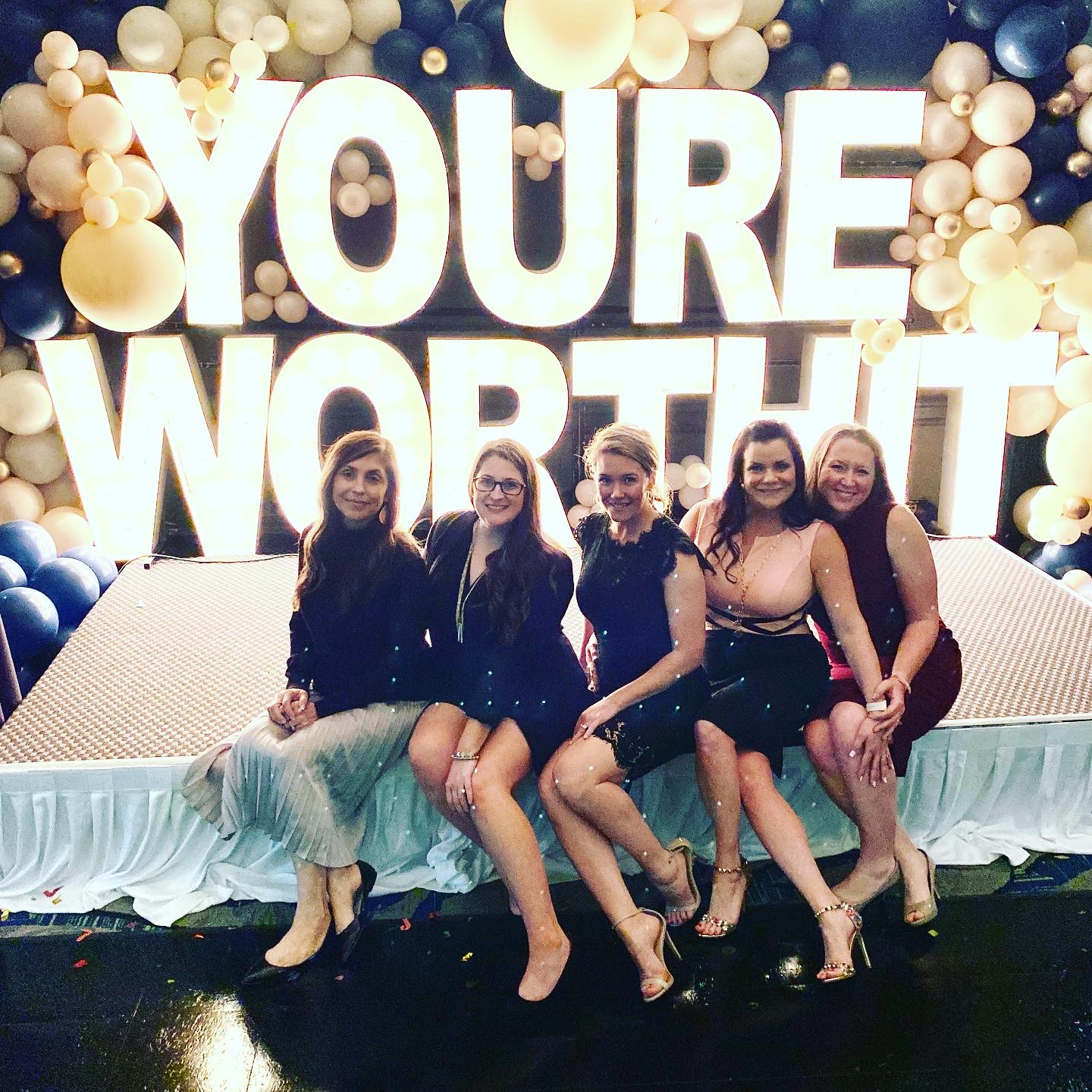 A group of ladies sitting in front of "you're worth it" sign.