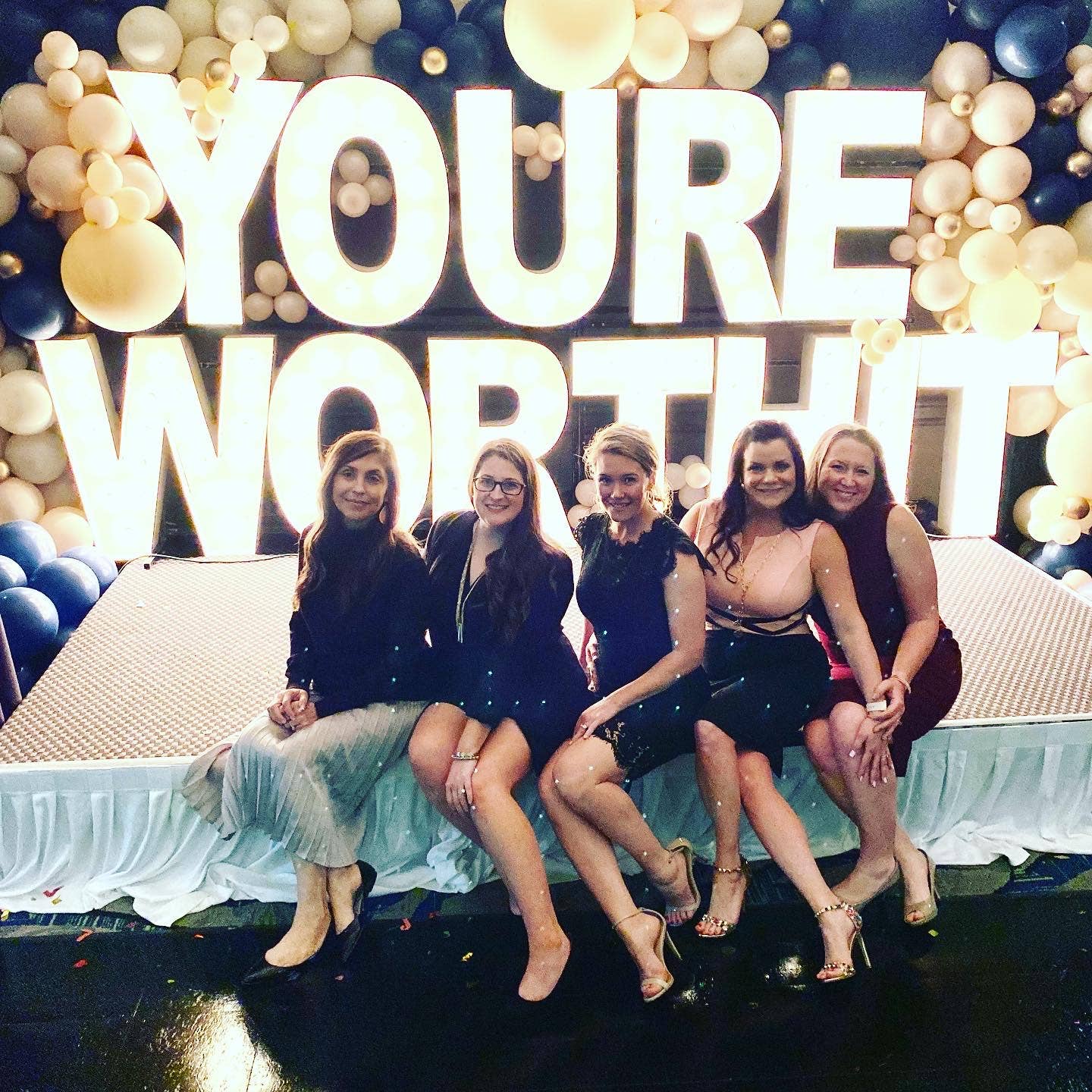 A group of ladies sitting in front of &quot;you're worth it&quot; sign.