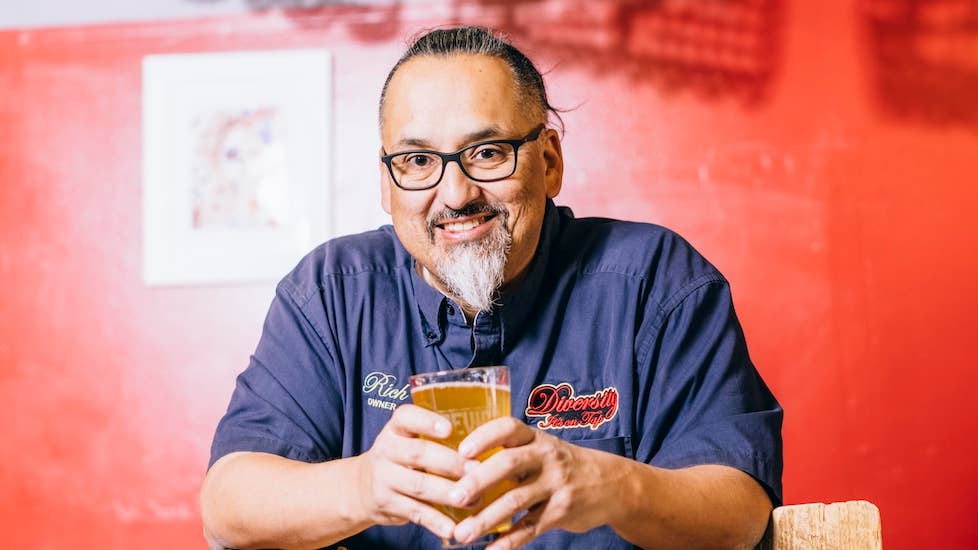 Richard Fierro standing in front of a red wall and holding a beer.