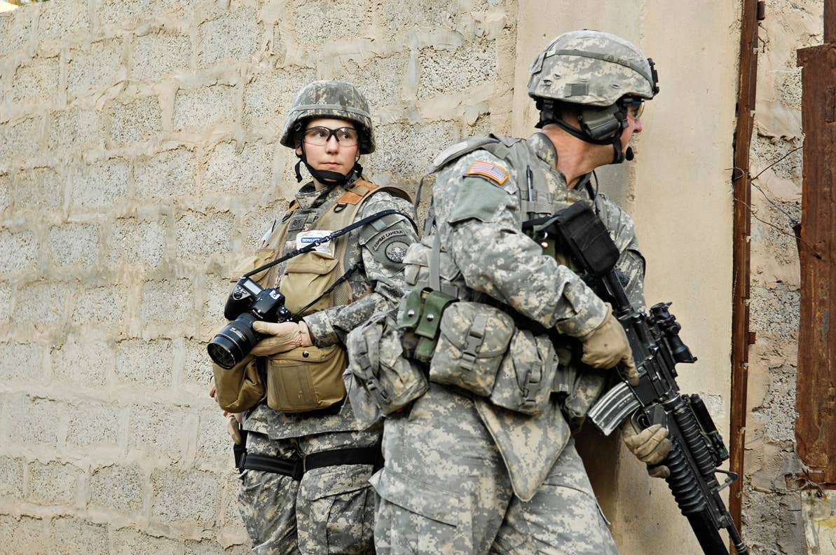 Stacy Pearsall in combat uniform next to soldier with rifle.
