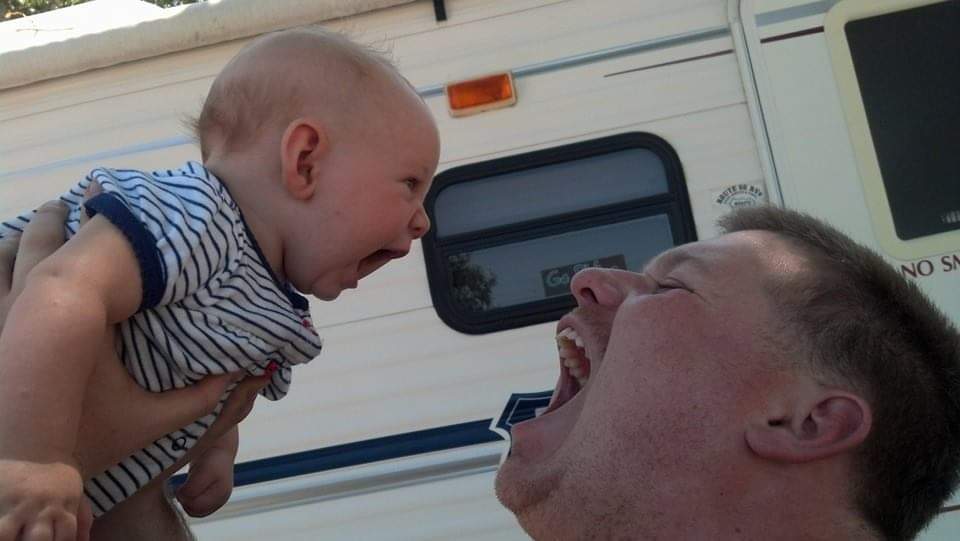 Charles Moore holding his young son in the air and laughing.