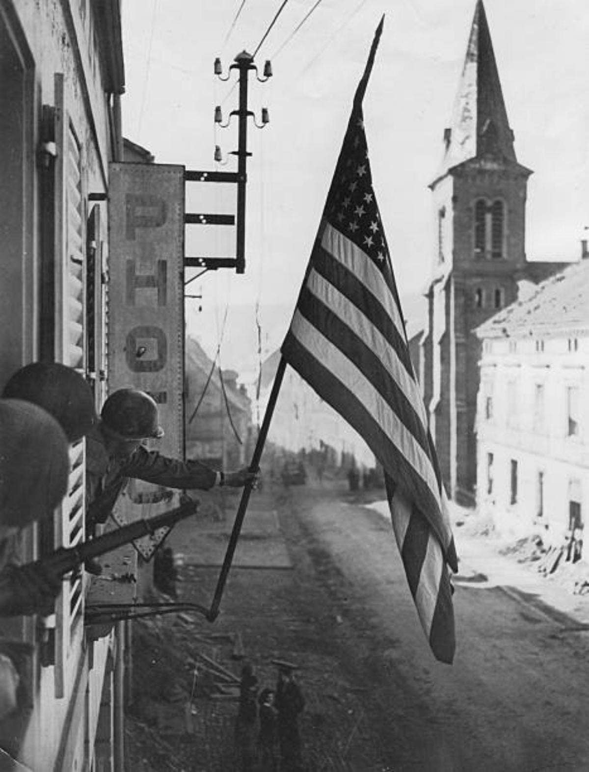 <em>A U.S. 7th Army soldier unfurls an American flag in Bitche, France (reddit.com/r/ww2)</em>