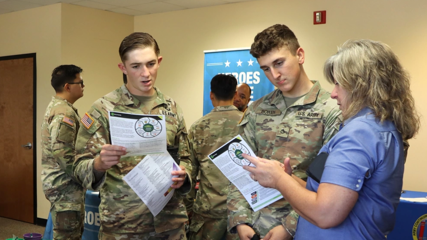 Two uniformed service members look at papers with a woman