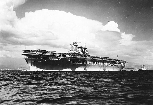 The U.S. Navy aircraft carrier USS <em>Yorktown</em> (CV-5) anchored in Haitian waters, circa 1938-1940. Note the Curtiss SOC <em>Seagull</em> taxiing off <em>Yortown</em>'s bow and the <em>New Mexico</em>-class battleship in the background.