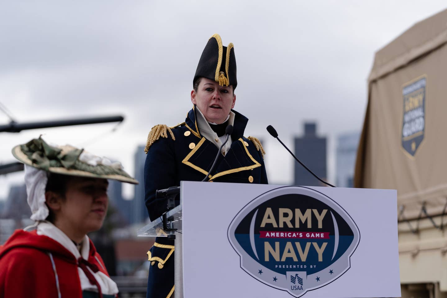 A woman speaks at a podium during the USAA Army-Navy game celebrations.