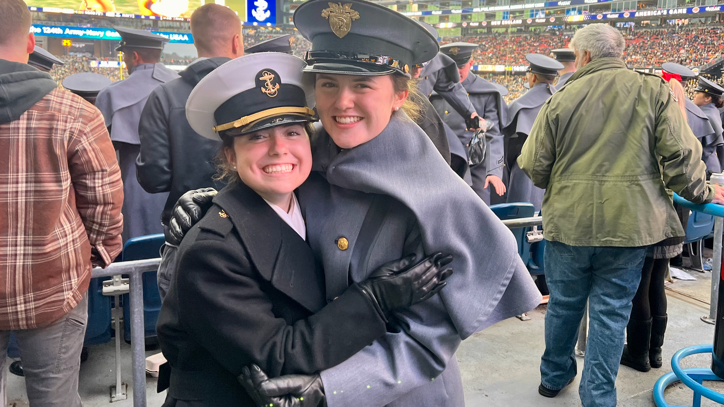 A Naval Academy midshipman and West Point cadet hug in the Gillette stadium