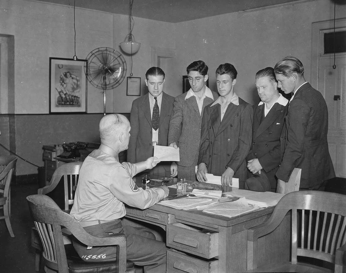 Five men stand before an Army recruiter at a desk in 1940