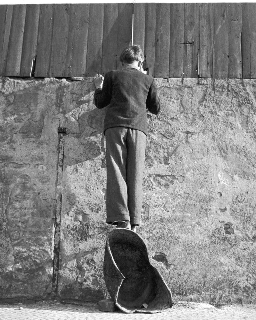 A boy stands on a coal scuttle to peer over the wall of a sports stadium in Berlin, 8th January 1951. (Photo by Keystone Features/Hulton Archive/Getty Images)