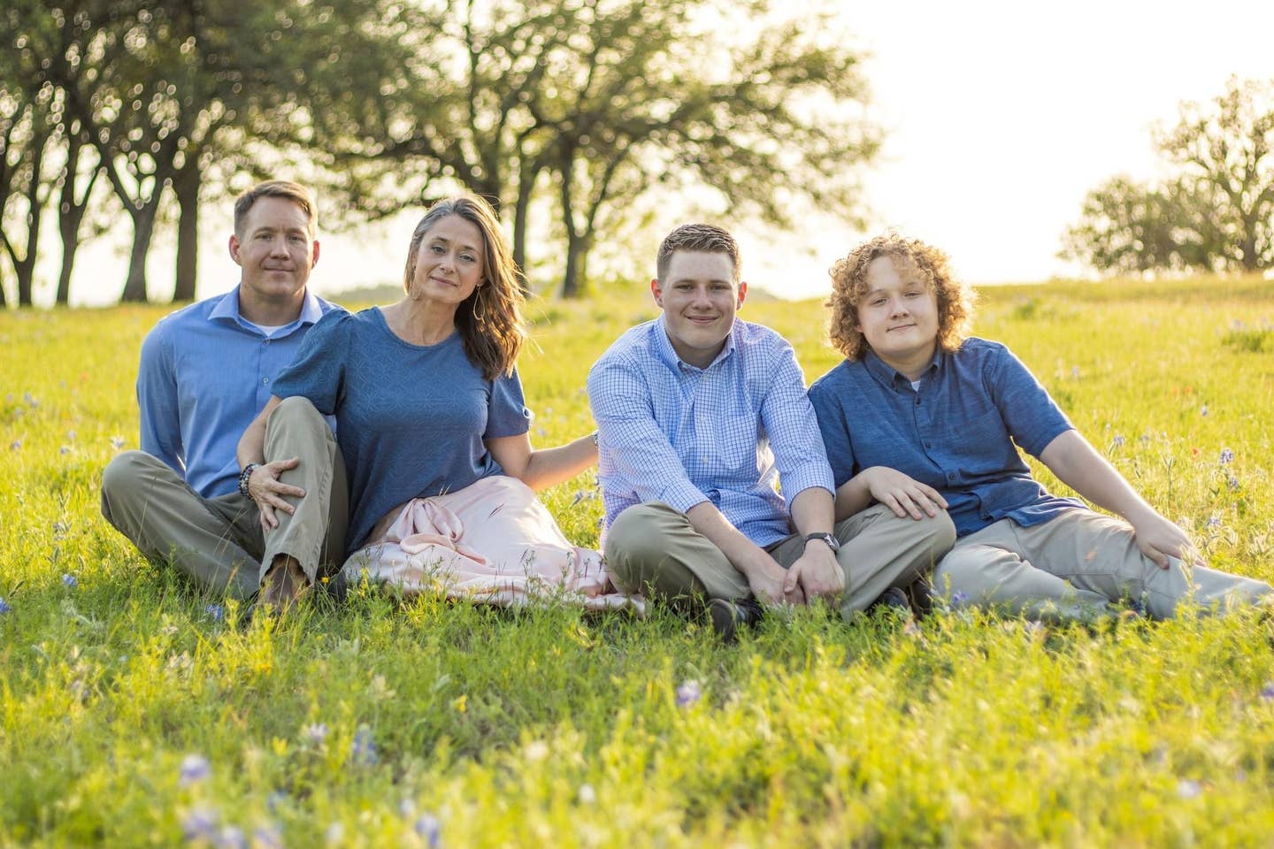 Corie Weathers poses with her husband and two sons, sitting in a field.