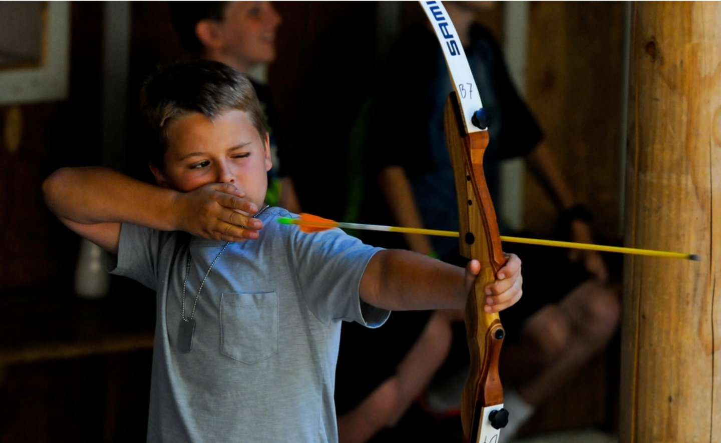 A boy aims a bow and arrow at summer camp