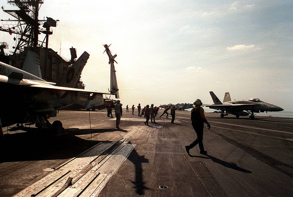 A U.S. Navy sailor walks on a flight deck of a battleship among jets